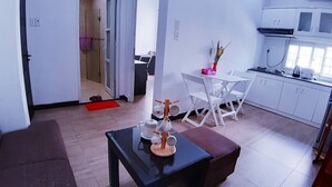 Un salón moderno con una mesa de centro negra, sillas blancas y una zona de cocina con armarios blancos y una estufa.