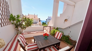 Eine kleine Terrasse im Freien mit Tisch und zwei Stühlen, einem Blumentopf und Blick auf das Meer.