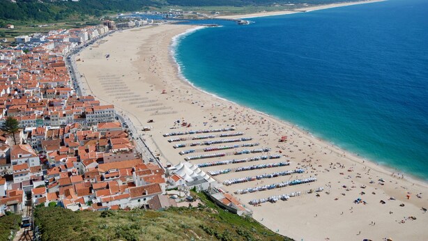 A coastal town with a long sandy beach, rows of beachside tents, and a dense cluster of red-roofed buildings along the shore. - Turtle - 3 bedroom apartment in Nazaré with 2 shared pools and private terrace (Nazaré)
