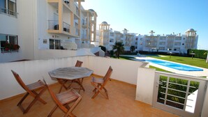 A balcony with a table and chairs, overlooking a swimming pool and a building with multiple floors and balconies. - Turtle - 3 bedroom apartment in Nazaré with 2 shared pools and private terrace (Nazaré)