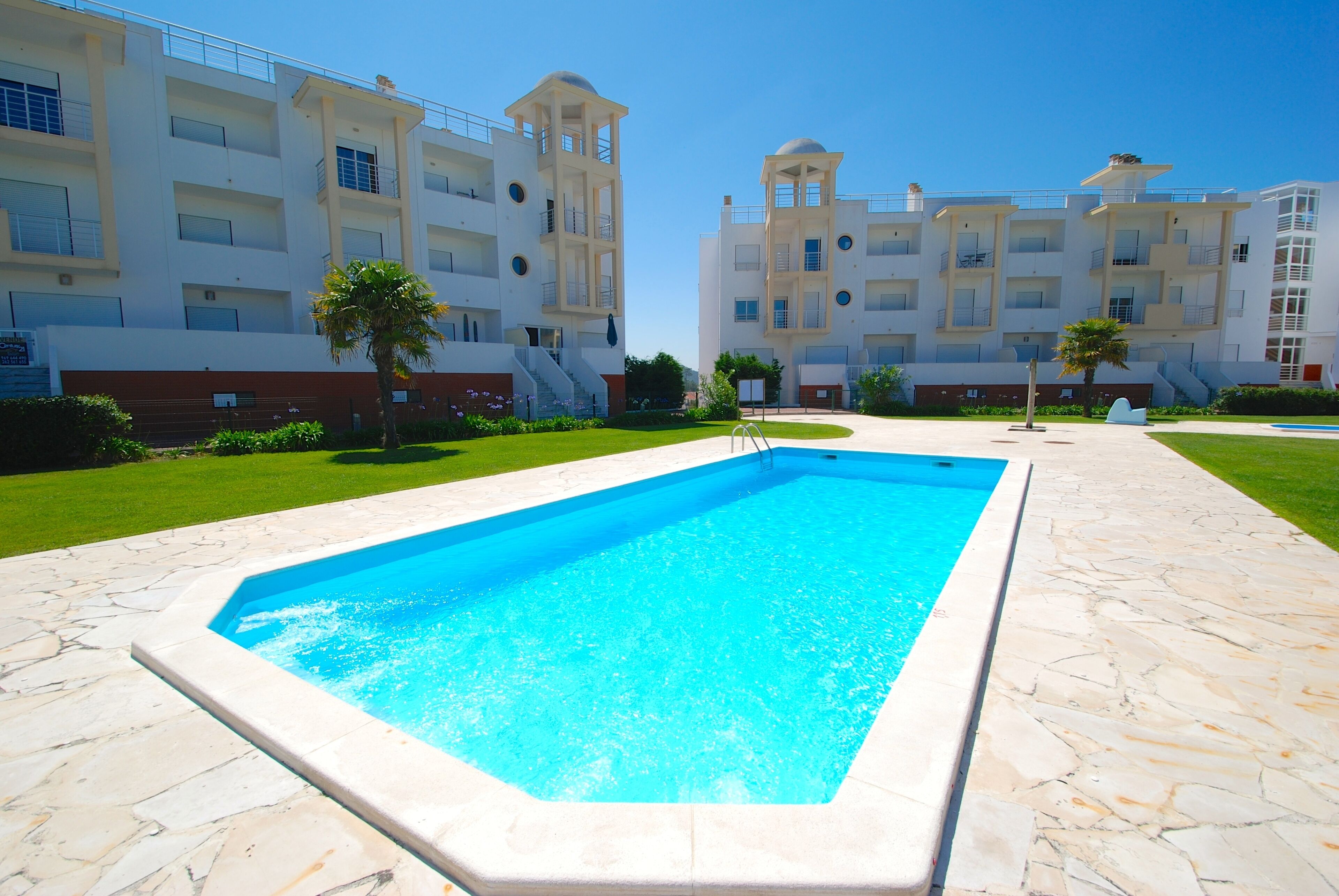 Una piscina rodeada de baldosas de piedra, con un edificio al fondo que presenta balcones y una estructura en forma de cúpula.