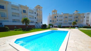 A swimming pool surrounded by stone tiles, with a building featuring balconies and a dome structure in the background. - Turtle - 3 bedroom apartment in Nazaré with 2 shared pools and private terrace (Nazaré)