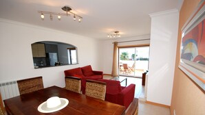 A dining area with a wooden table, red upholstered chairs, a white hat on the table, and a view of the outdoors through a glass door. - Turtle - 3 bedroom apartment in Nazaré with 2 shared pools and private terrace (Nazaré)