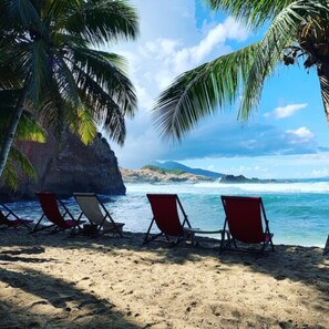 A beach with red lounge chairs and a palm tree. - Escape Boutique Hotel and Beach Bar (Calibishie)