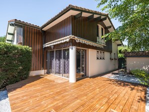 Ein zweistöckiges Haus mit einer Holzdachterrasse, großen Schiebeglastüren und einem Ziegeldach.