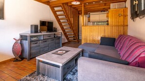 Una sala de estar acogedora con techo de madera, un sofá, una mesa de centro y un televisor sobre un mueble.