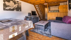 Una habitación acogedora con techo de madera, una mesa de comedor con mantel estampado, un sofá gris y una pequeña mesa de centro.