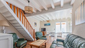 A spacious living room with a staircase, green leather sofas, a wooden coffee table, and a dining area with white chairs. - Spacious 3-BR House, Sleeps 7, Near Beach & Town, Large Yard, BBQ, Pet-Friendly (Biscarrosse Plage)