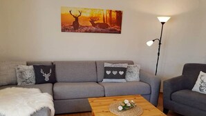 Un salon avec un canapé gris, une table basse en bois et un tableau représentant des cerfs accroché au mur.
