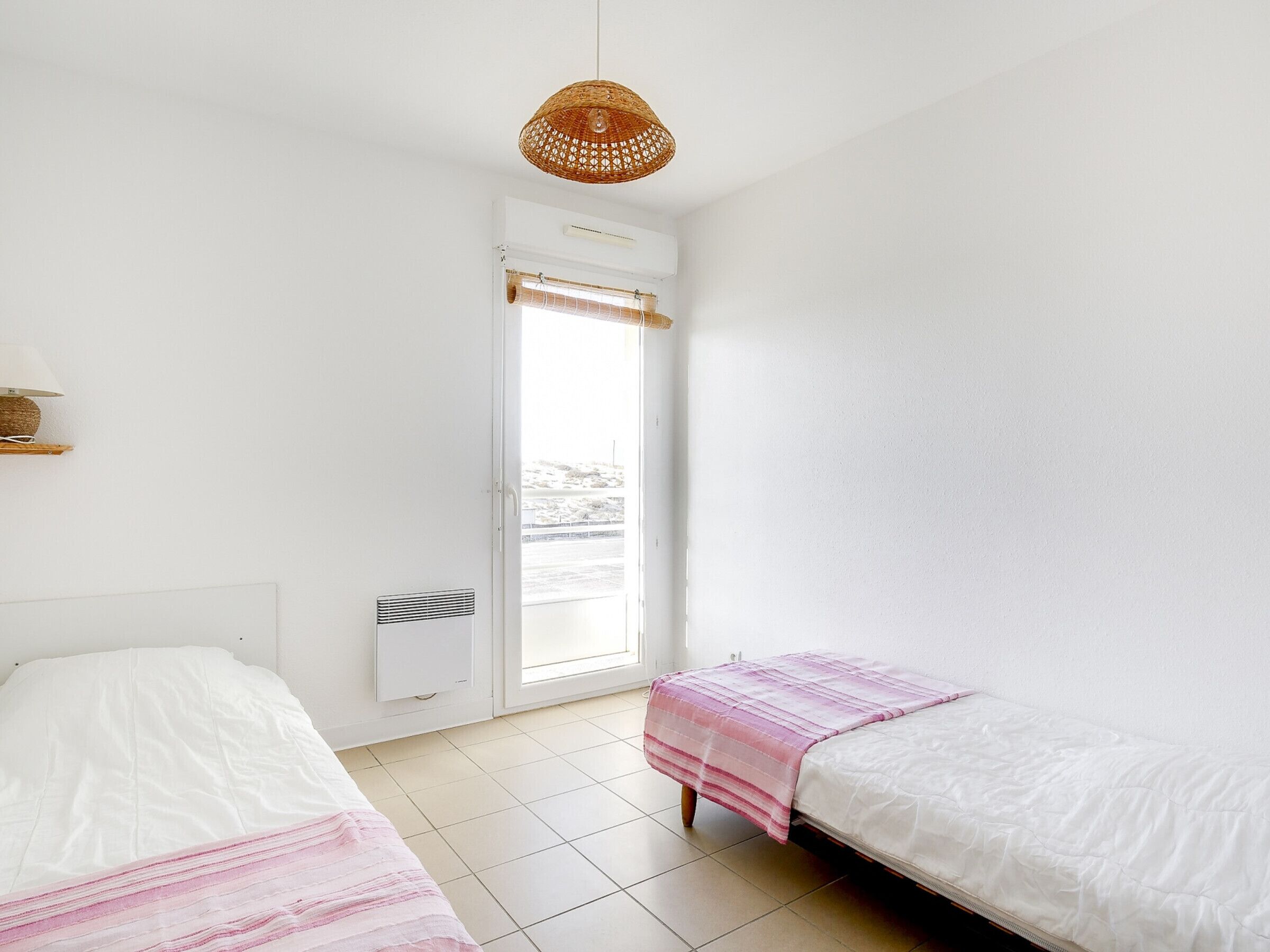 Una habitación con dos camas, una ventana con vistas, una lámpara en el techo y un calefactor de pared.
