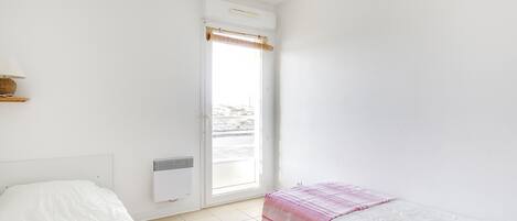 Una habitación con dos camas, una ventana con vistas, una lámpara en el techo y un calefactor de pared.