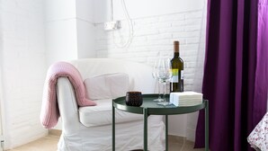 A white sofa with a pink blanket, a green table with a bottle of wine, a glass, and a candle. - Aladdin's Hostel (Larnaca)