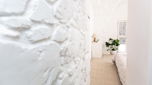 A room with a white textured wall, a bed with a floral bedspread, a bedside table with a lamp, and a potted plant. - Aladdin's Hostel (Larnaca)