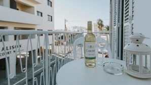 A balcony with a white table, a bottle of Carosol wine, a glass, and a white lantern. - Aladdin's Hostel (Larnaca)