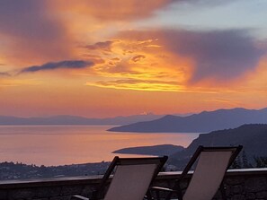 A sunset view from a balcony with lounge chairs, overlooking a calm body of water and distant mountains. - Villa Phoebe in Stoupa, very quiet area, private pool, spectacular sea views. (Stoupa,)