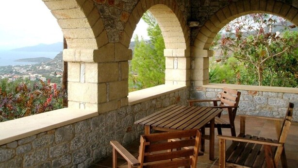 Un'area salotto esterna ad arco in pietra con tavolo e sedie, affacciata su un paesaggio pittoresco.