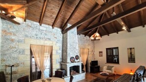 Un accogliente soggiorno con parete in pietra, camino, zona pranzo con tavolo e sedie e un divano.