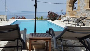 Area piscina con due poltronghe da relax e un tavolo, con vista panoramica sul mare e sulle montagne.