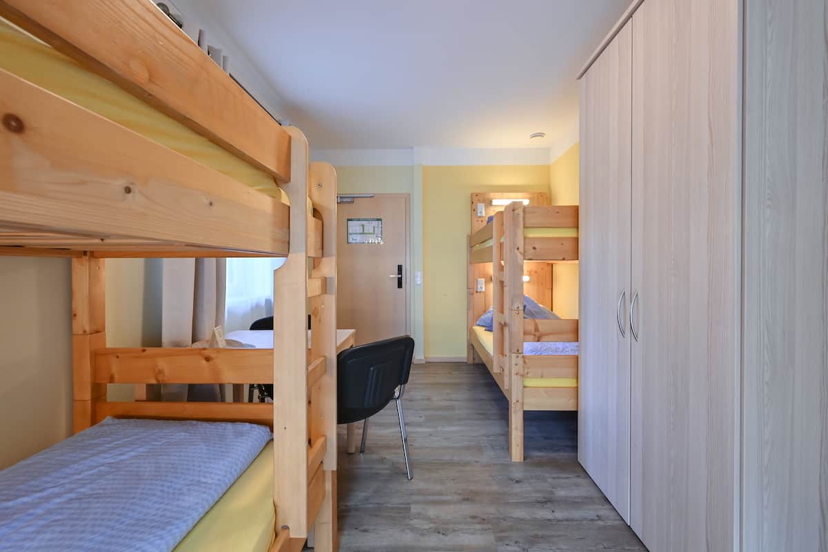 A narrow corridor with bunk beds on both sides, a desk with a chair, and a wardrobe.