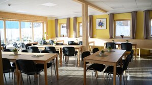 A dining area with multiple tables and chairs, large windows with curtains, and a view of the outside.