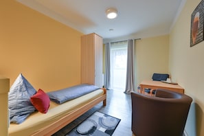A small, well-lit room with a single bed, a chair, a desk, and a wardrobe. - Rote Villa Füssen (Fuessen)