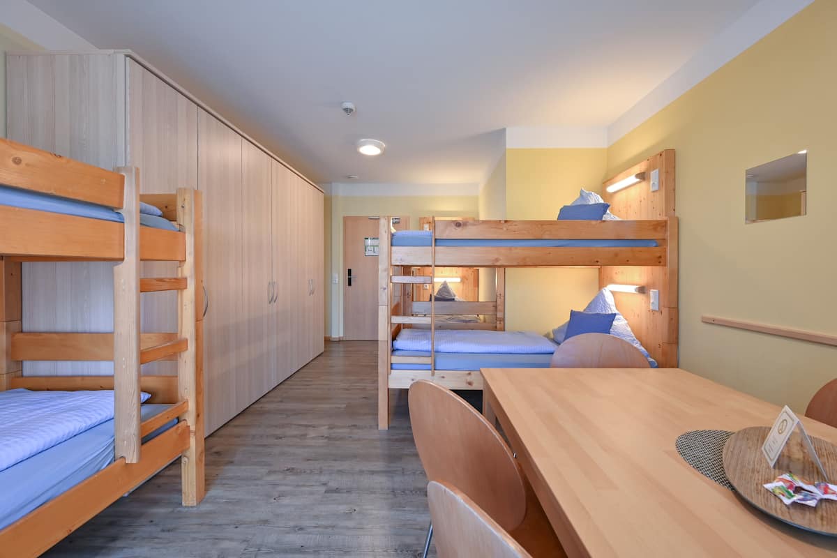 A dormitory room with bunk beds, a wooden desk, and a chair.