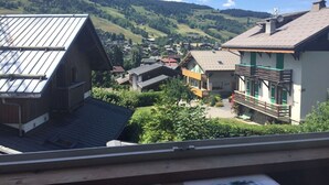 A residential area with houses featuring sloped roofs and balconies, surrounded by lush green hills and a clear blue sky. - MEGEVE-T2-44M²-NEAR TOWN CENTER (Megève)