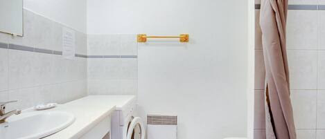 Une petite salle de bain comprenant un lavabo, un lave-linge, des toilettes et un porte-serviettes.