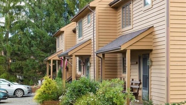 Een rij houten vakantiehuisjes met aanbouwen, omringd door groen en parkeerplaatsen.