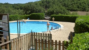 A swimming pool surrounded by a wooden fence, with a wooden deck in the foreground and a wooded area in the background. - Chalet Acanthe (Simiane-la-Rotonde)
