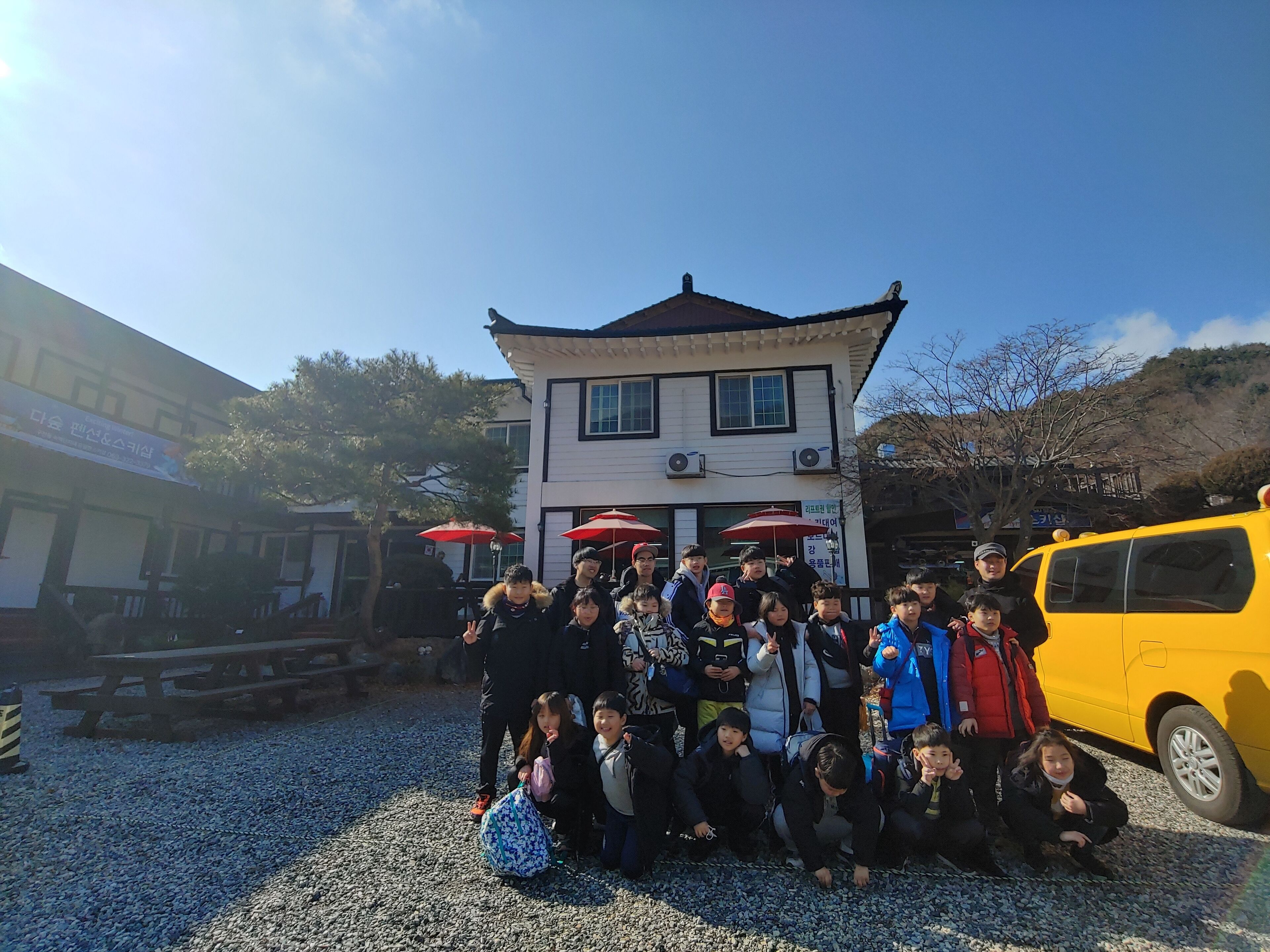 A group of people posing in front of a traditional building with a tiled roof, surrounded by gravel.