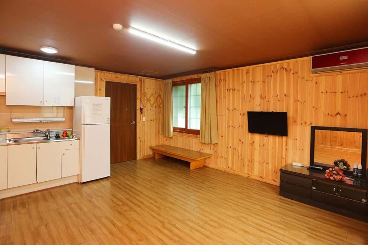 A compact kitchen with wooden walls, a bench, and a TV on a wooden cabinet.