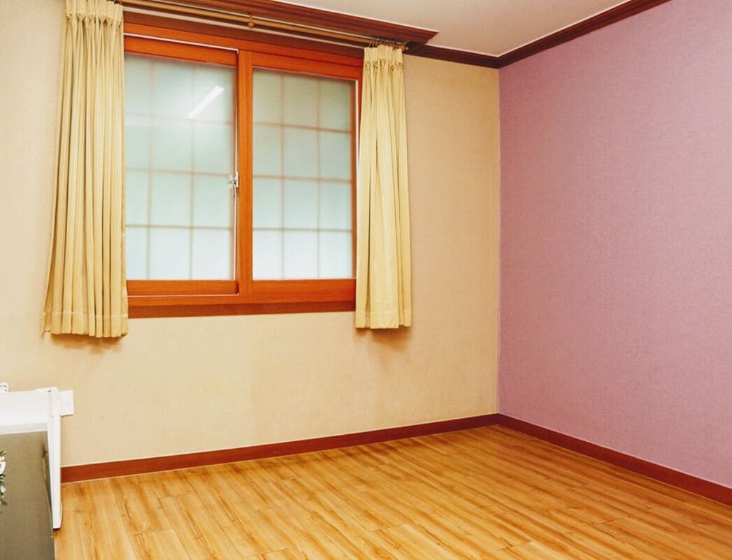 Ein Zimmer mit Holzboden, einem fenster mit Vorhängen und einer violetten Wand.