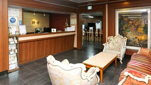 A hotel lobby with a reception desk, seating area, and a painting on the wall.