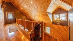 A wooden interior with a sloped ceiling, a wooden staircase, and a deer head mounted on the wall.