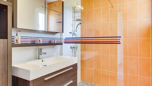 A modern bathroom with a white sink, wooden vanity, and a glass shower enclosure. - Modern Home with Terrace in Biscarrosse – Sleeps 7 with WiFi & BBQ (Biscarrosse)