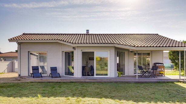 A single-story house with a tiled roof, a covered patio with outdoor furniture, and a sliding glass door leading to a patio area. - Modern Home with Terrace in Biscarrosse – Sleeps 7 with WiFi & BBQ (Biscarrosse)