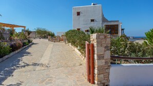 A stone-paved pathway leading to a white building with a balcony overlooking a beach. - Armonia Studios and Villas (Naxos)