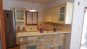 A kitchen with a stone island, wooden cabinets, and a stainless steel refrigerator. - Armonia Studios and Villas (Naxos)