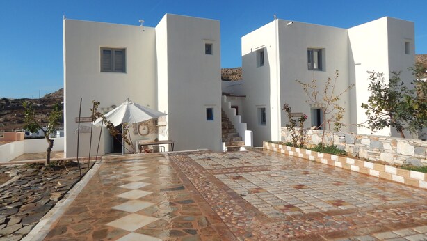 A modern building with a tiled courtyard, a staircase, and a small table with an umbrella. - Armonia Studios and Villas (Naxos)