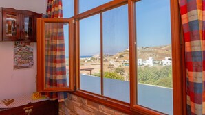A room with a large window overlooking a coastal landscape, a wooden cabinet, and a poster on the wall. - Armonia Studios and Villas (Naxos)