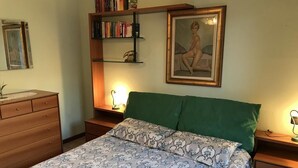 A bedroom with a bed, a dresser, a nightstand, a bookshelf, and a framed picture on the wall. - Apartment with garden and parking (Edolo)