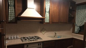 A kitchen with wooden cabinets, a gas stove, an oven, a sink, and a window with a curtain. - Apartment with garden and parking (Edolo)