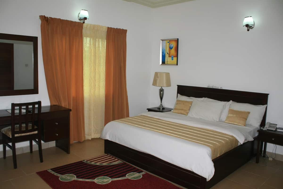 A hotel room with a bed, desk, chair, lamp, and artwork on the wall.