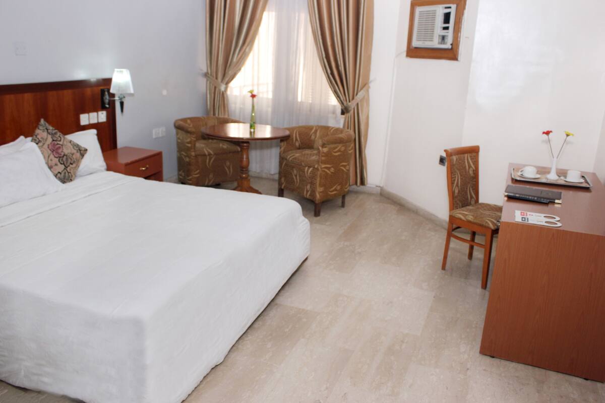 A hotel room with a bed, a desk, two chairs, a small table, and curtains.
