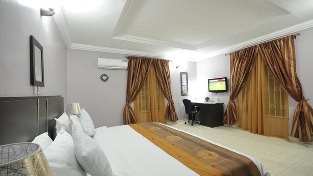 Quarto de hotel com uma cama, escrivaninha, cadeira, cortinas, televisão e aparelho de ar condicionado.