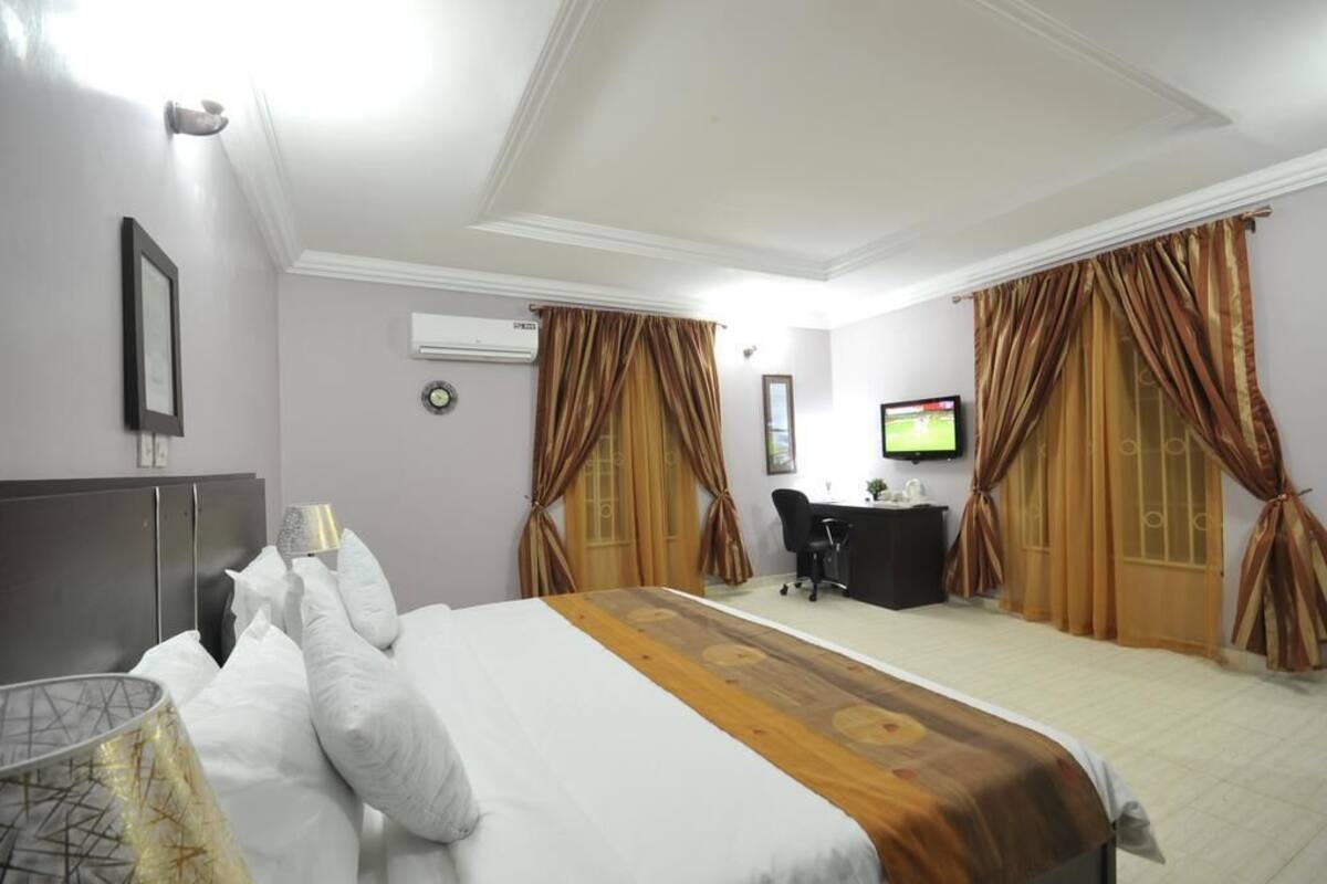 A hotel room with a bed, a desk, a chair, curtains, a television, and an air conditioning unit.