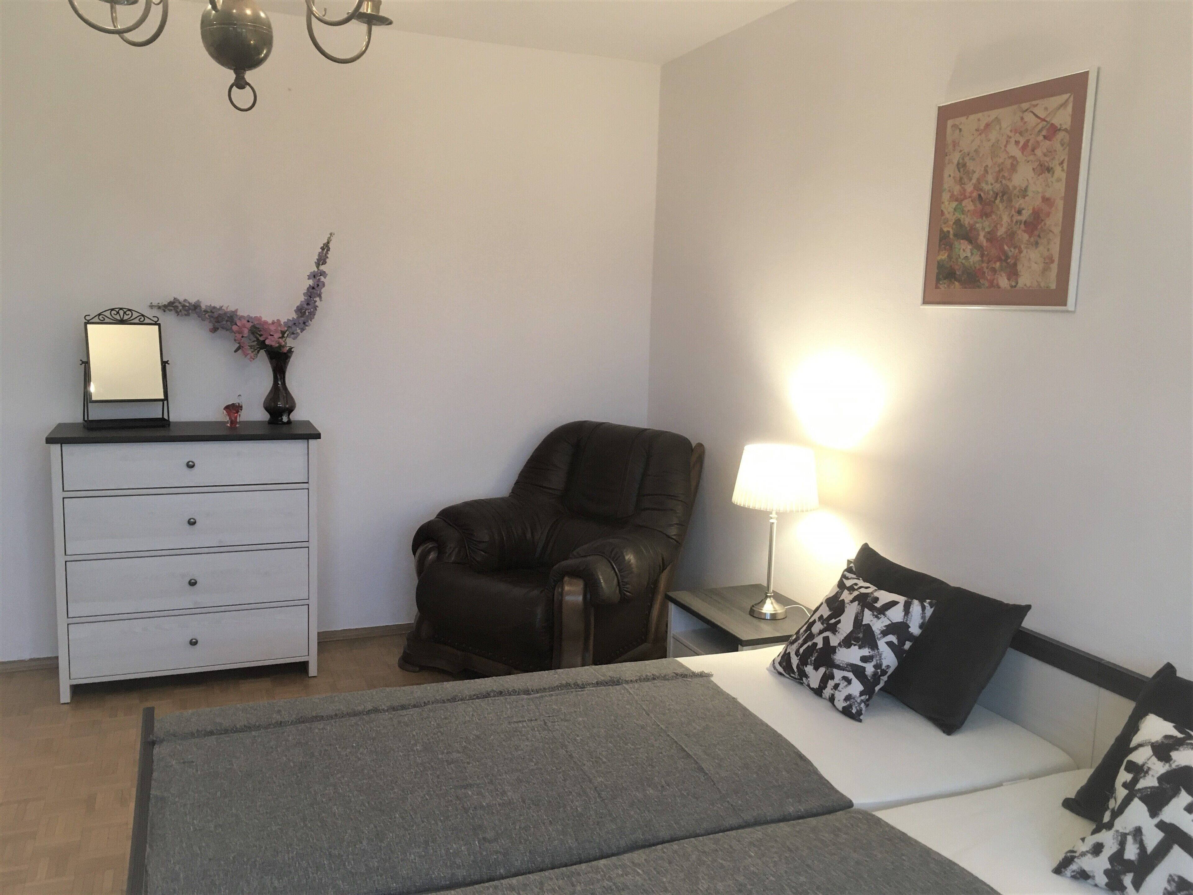 A bedroom with a bed, a chair, a dresser, a lamp, and a painting on the wall.