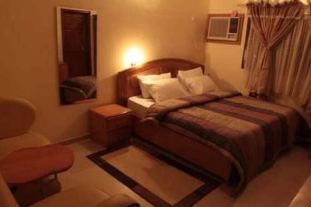 Une chambre d’hôtel avec un lit, une table de chevet, une chaise et une fenêtre avec des rideaux.