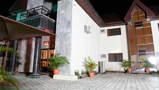 Un hotel con un patio central, una entrada amplia con puerta de cristal y numerosas plantas en macetas.